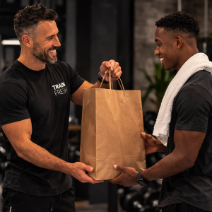 Fitness coach handing a large brown paper bag containing cleaned sneakers to an athlete in a gym